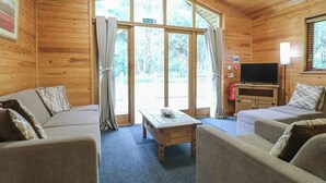 A cozy cabin interior with a sofa, armchairs, a coffee table, and a television. - Rowan Lodge (Swadlincote)