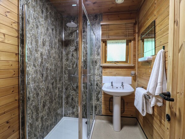 Baño de cabaña de madera con ducha envuelta en vidrio, un lavamanos blanco y un espejo encima.