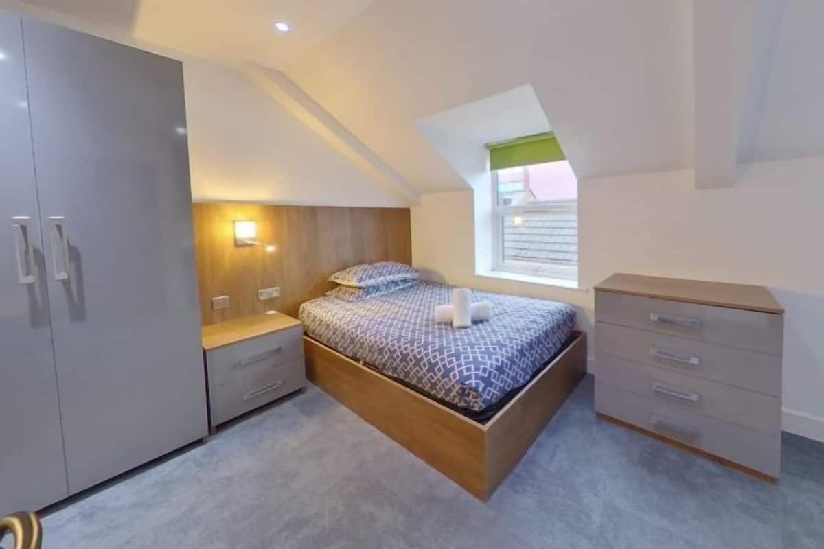 A bedroom with a loft bed, a wardrobe, a bedside table, and a window with a view.