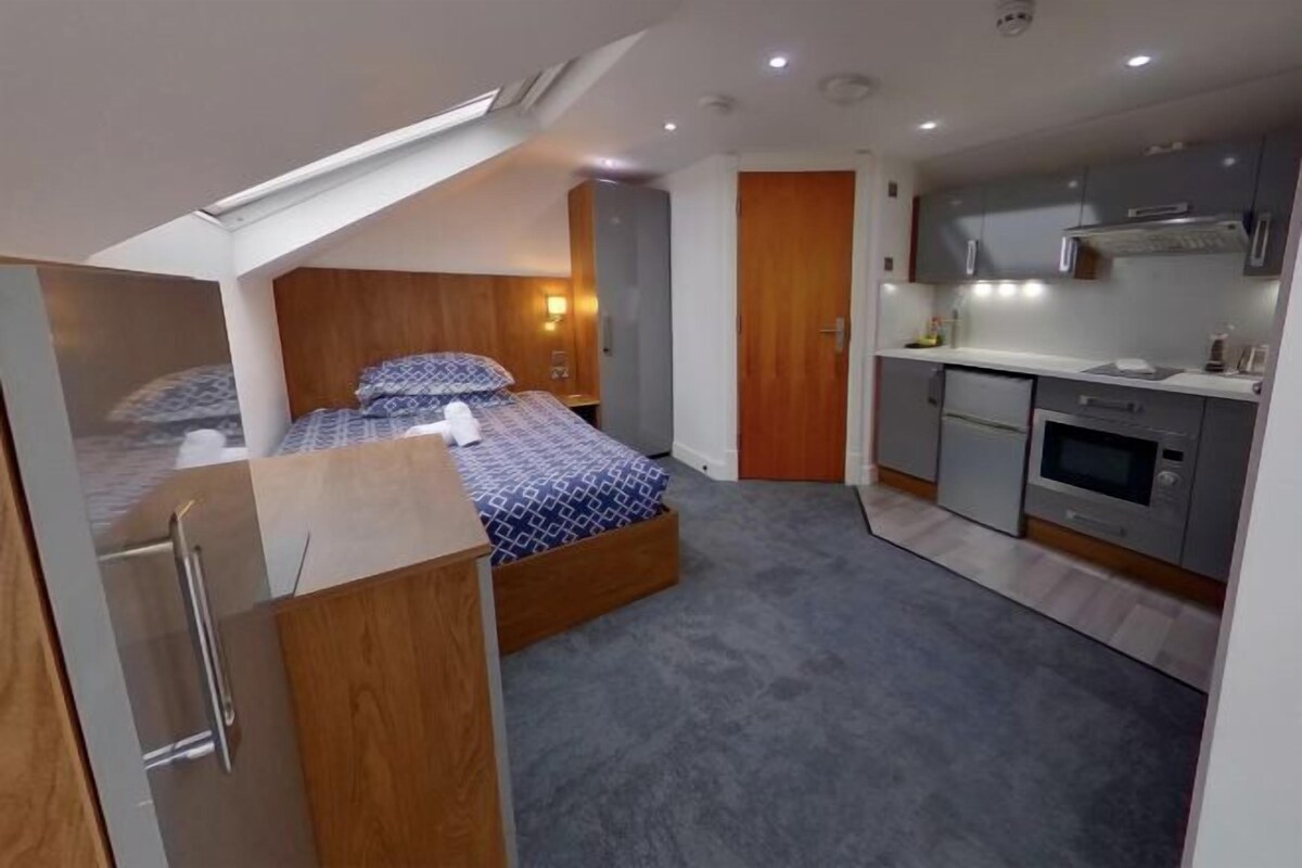 A compact bedroom with a bed, a small kitchenette, and a wooden wardrobe.