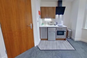A compact kitchen with a microwave, oven, and small refrigerator. - CovStays – Victoria House - Deluxe Studios in Coventry City Centre (Coventry)