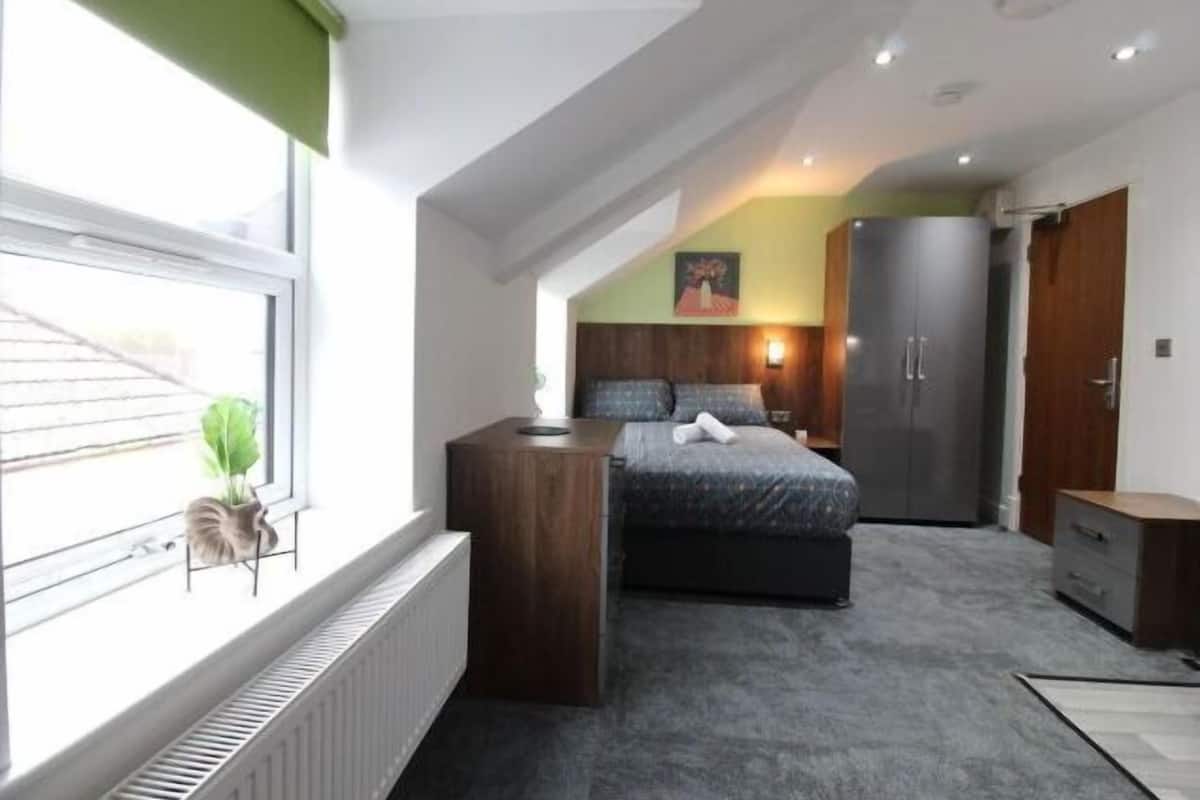 A bedroom with a bed, a radiator, a window, a plant, and a wardrobe.