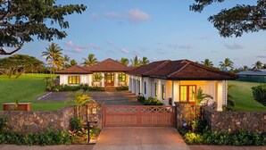 A two-story house with a stone wall entrance, a driveway leading to the front door, and a well-maintained lawn. - Perfection in Poipu:  Brand new luxury home, ocean views, pool+spa (Koloa)