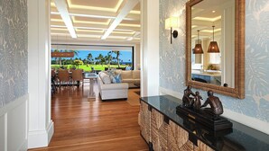 A modern living room with a wooden floor, a large mirror, and a view of a golf course. - Perfection in Poipu:  Brand new luxury home, ocean views, pool+spa (Koloa)