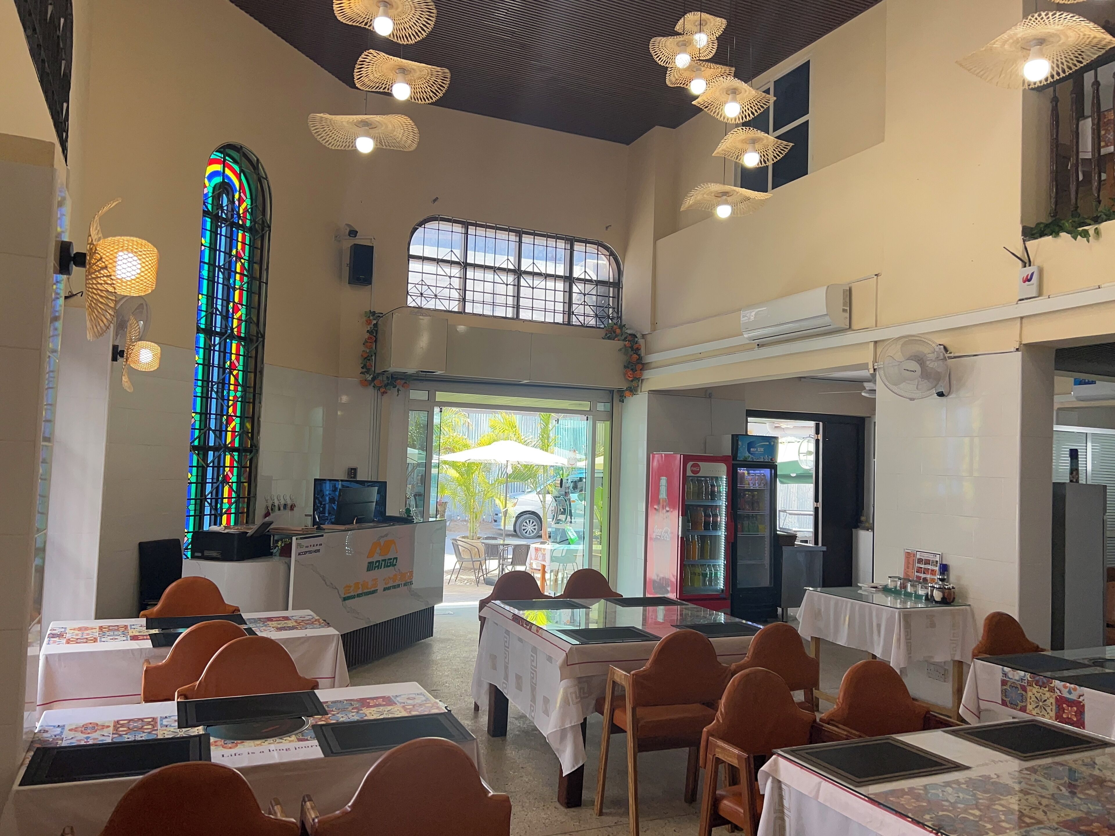A restaurant with tables and chairs, a stained glass window, and ceiling fans.