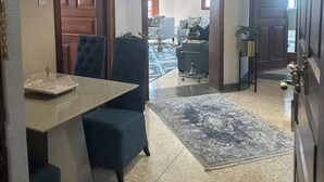 A spacious living area with a dining table, blue armchairs, and a coffee table. A hallway leads to a dining room with a chandelier. - Mango restaurant and apartment hotel (Zanzibar Town)