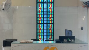 A reception desk with a stained glass window, a fan, and a sign for Mango Restaurant and Apartment Hotel. - Mango restaurant and apartment hotel (Zanzibar Town)