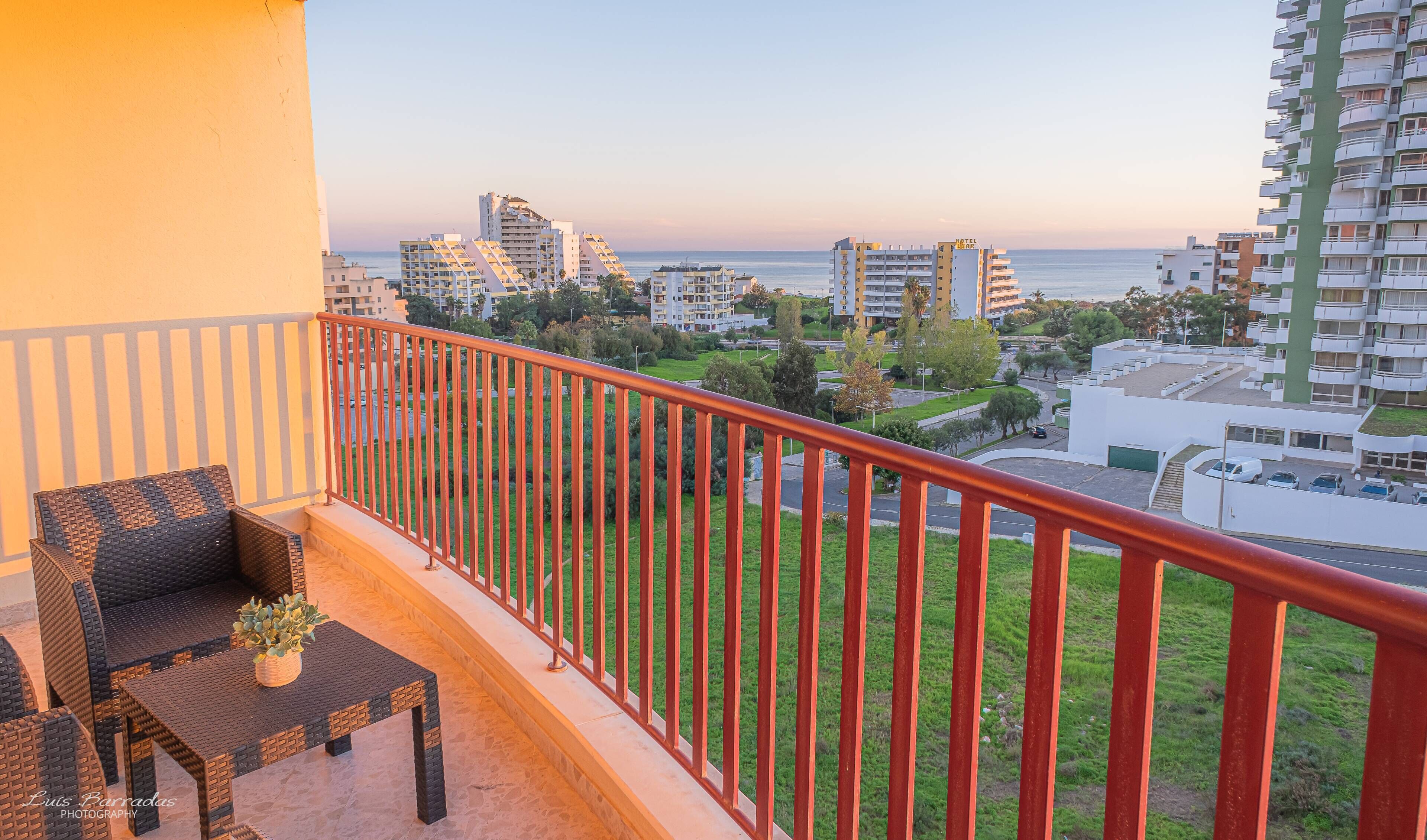 A balcony with wicker furniture and a view of the sea and surrounding buildings.