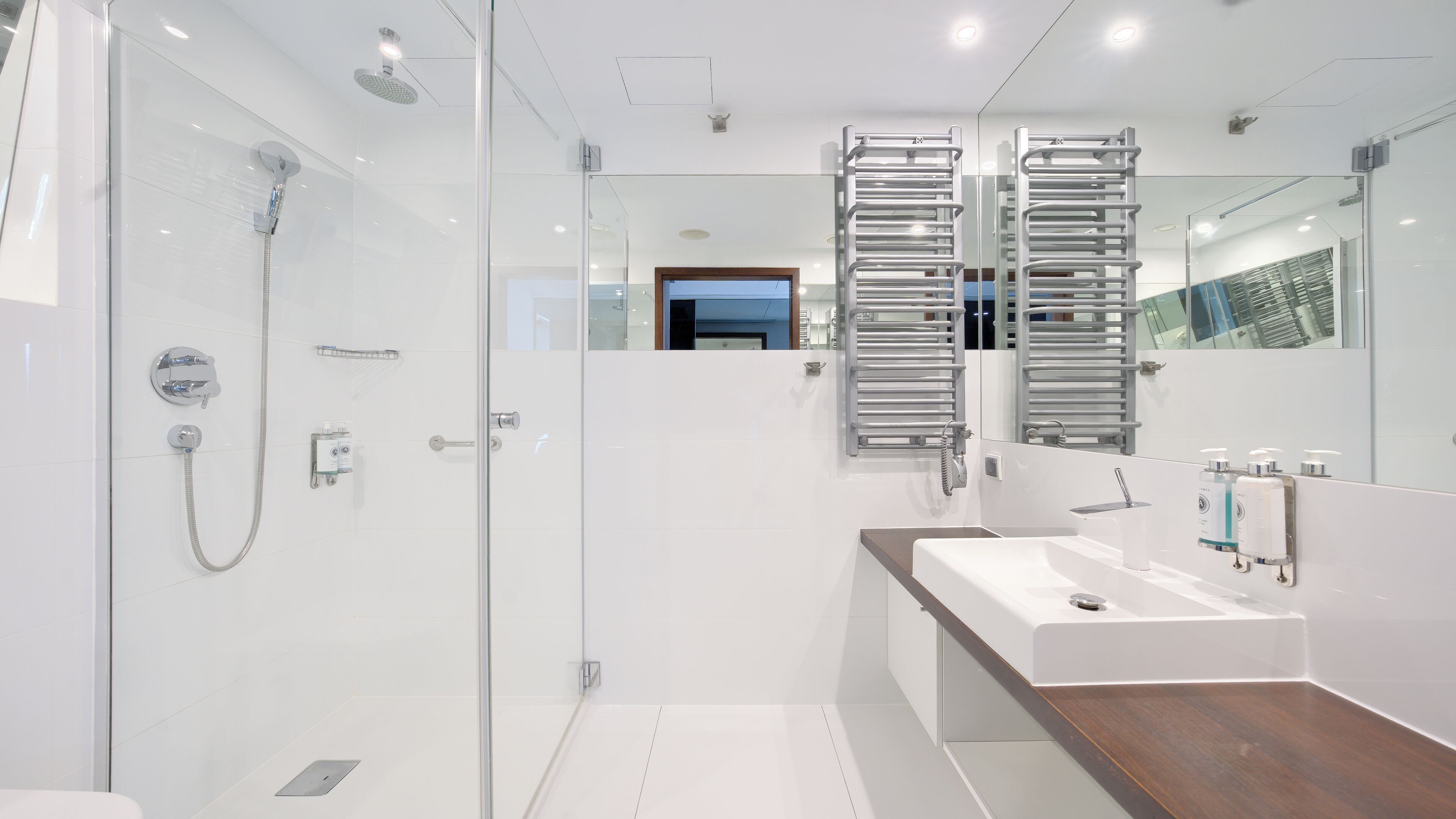 Een moderne badkamer met een douchecabine van glas, een witte wastafel met houten aanrechtblad en twee handdoekrekken.