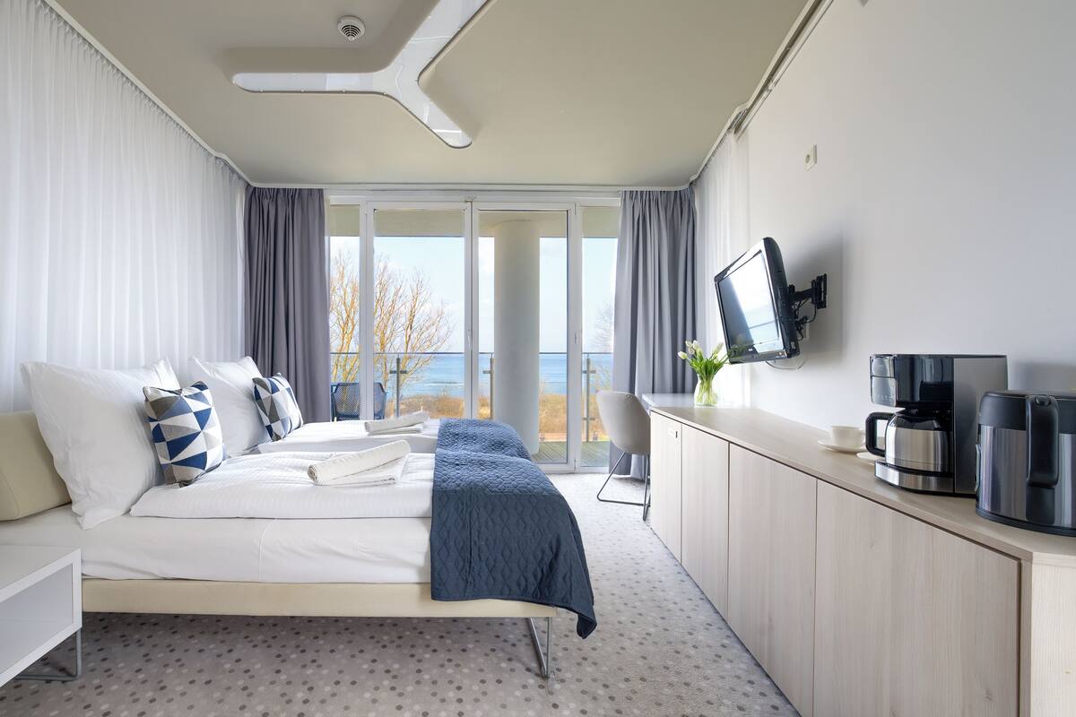 A modern hotel room with a bed, a desk, a coffee maker, and a TV.
