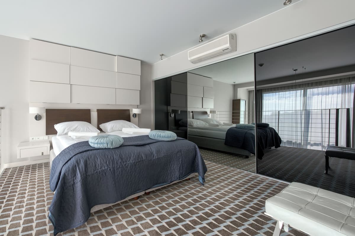 A modern hotel room with a large bed, a mirror, and a view of the cityscape.