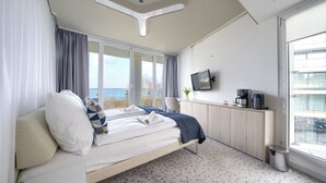A modern hotel room with a bed, a desk, a television, and a view of the sea. - Apartamenty Sun & Snow Marine (Kolobrzeg)