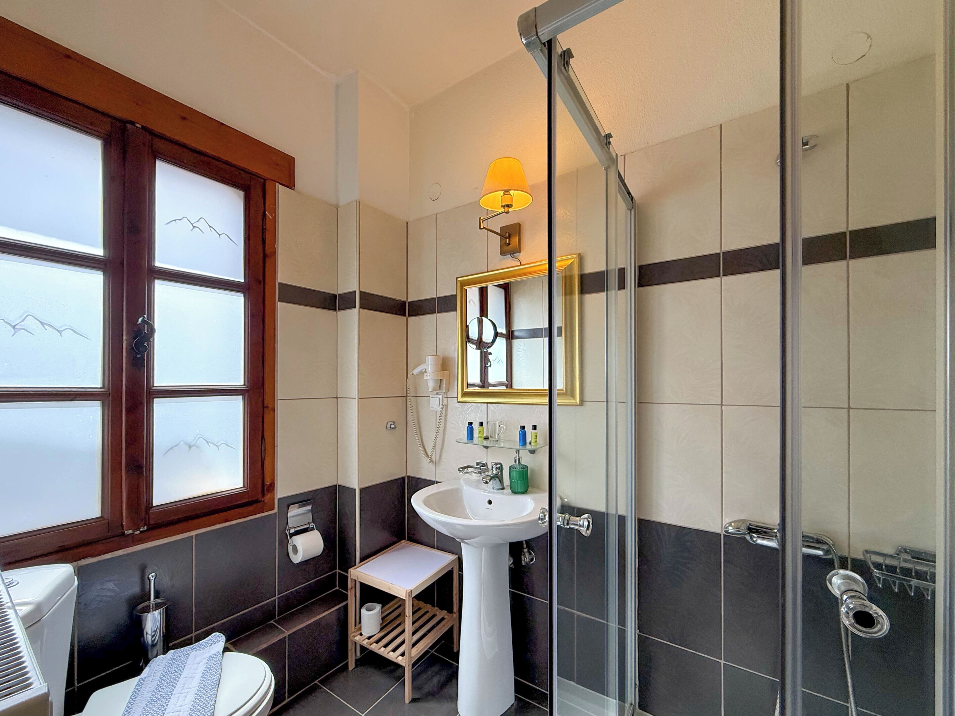 A bathroom with a toilet, sink, and shower. There is a window with frosted glass and a mirror above the sink.