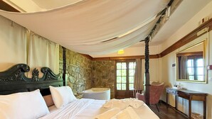 Une chambre à coucher avec un grand lit, un mur en pierre, une chaise en bois, un bureau et un miroir.