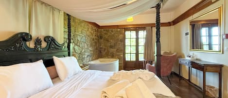 Un dormitorio con una cama grande, una pared de piedra, una silla de madera, un escritorio y un espejo.