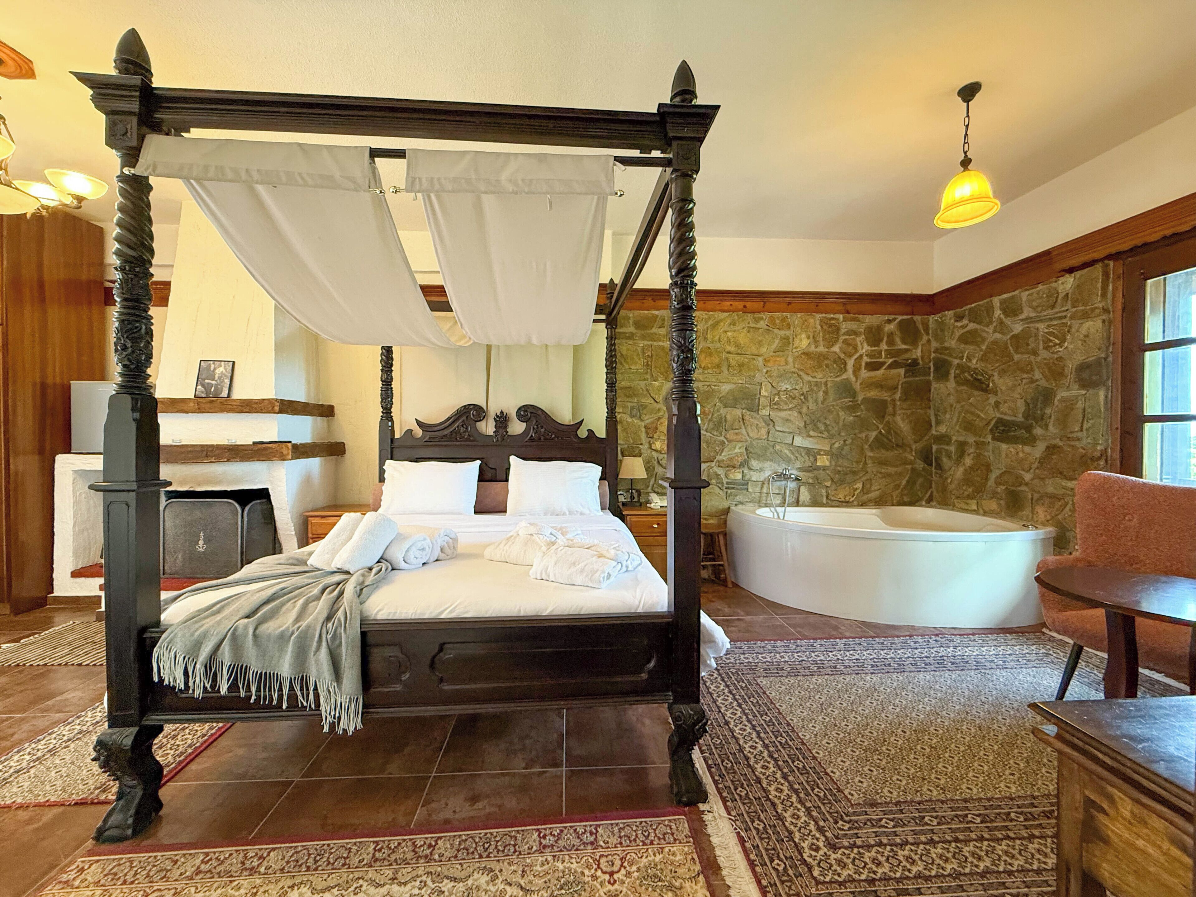 Uma cama com dossel e cortina, parede de pedra e banheira em quarto com piso de madeira e tapete estampado.