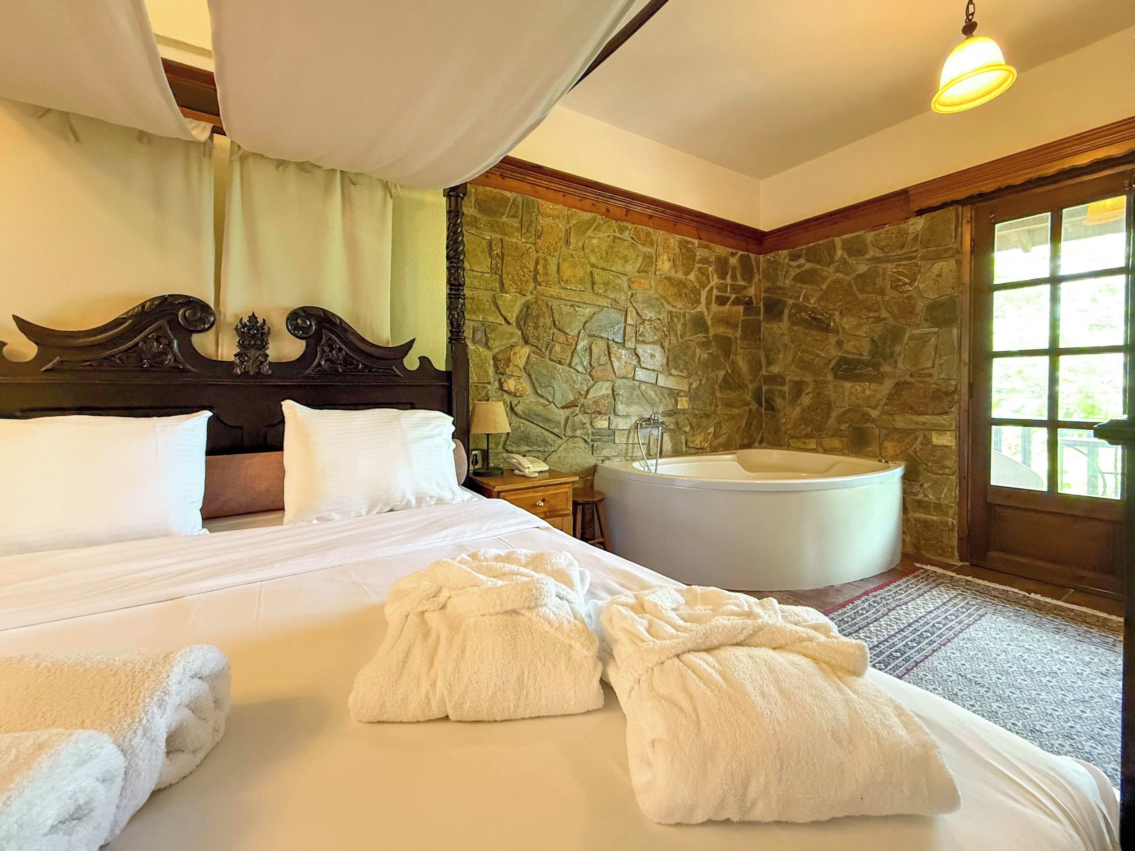 A hotel room with a large bed, a stone wall, a bathtub, and a window.