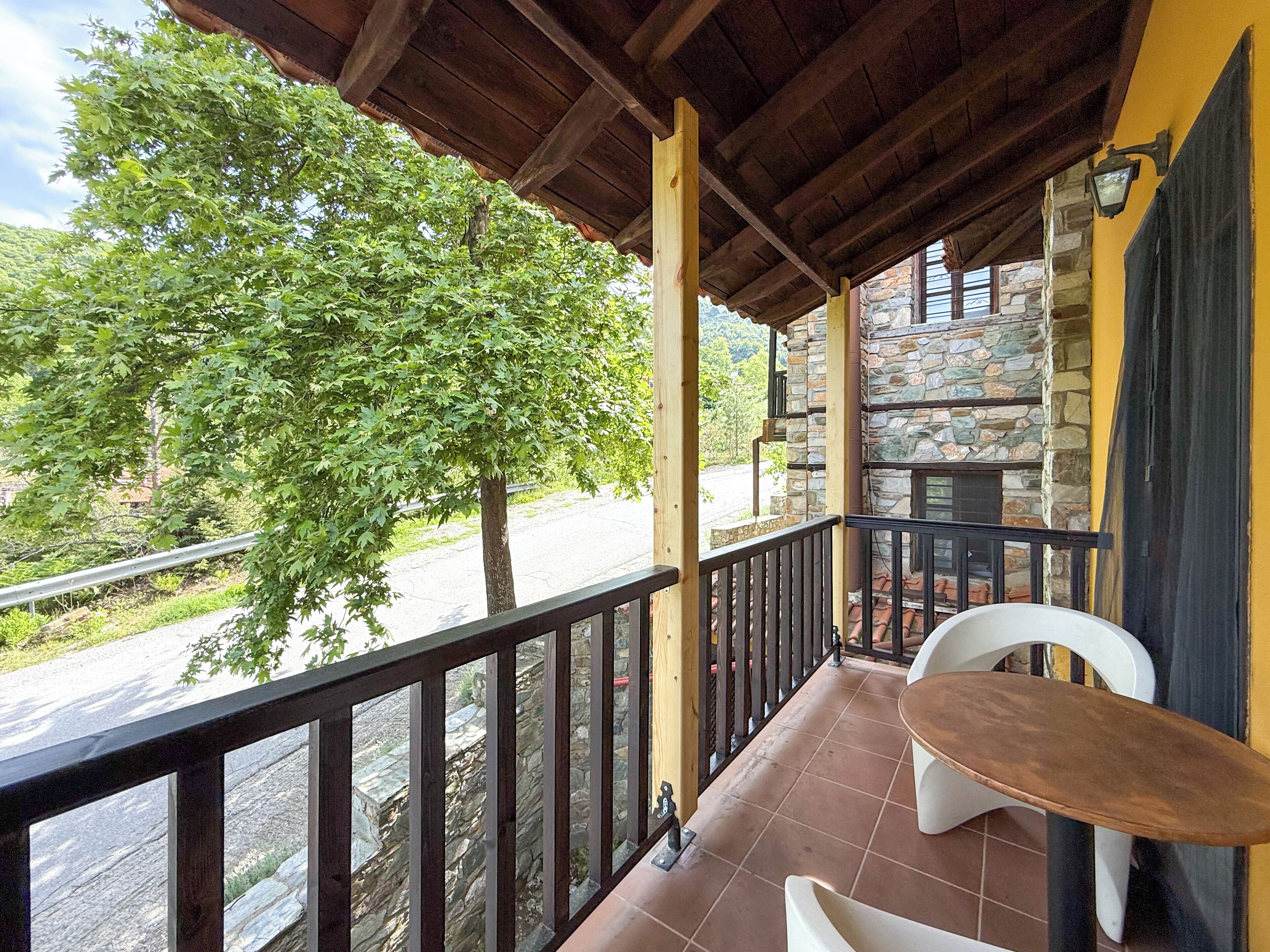 A balcony with a wooden railing, a stone wall, and a view of a tree and road.