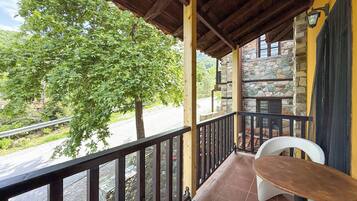 A balcony with a wooden railing, a stone wall, and a view of a tree and road.