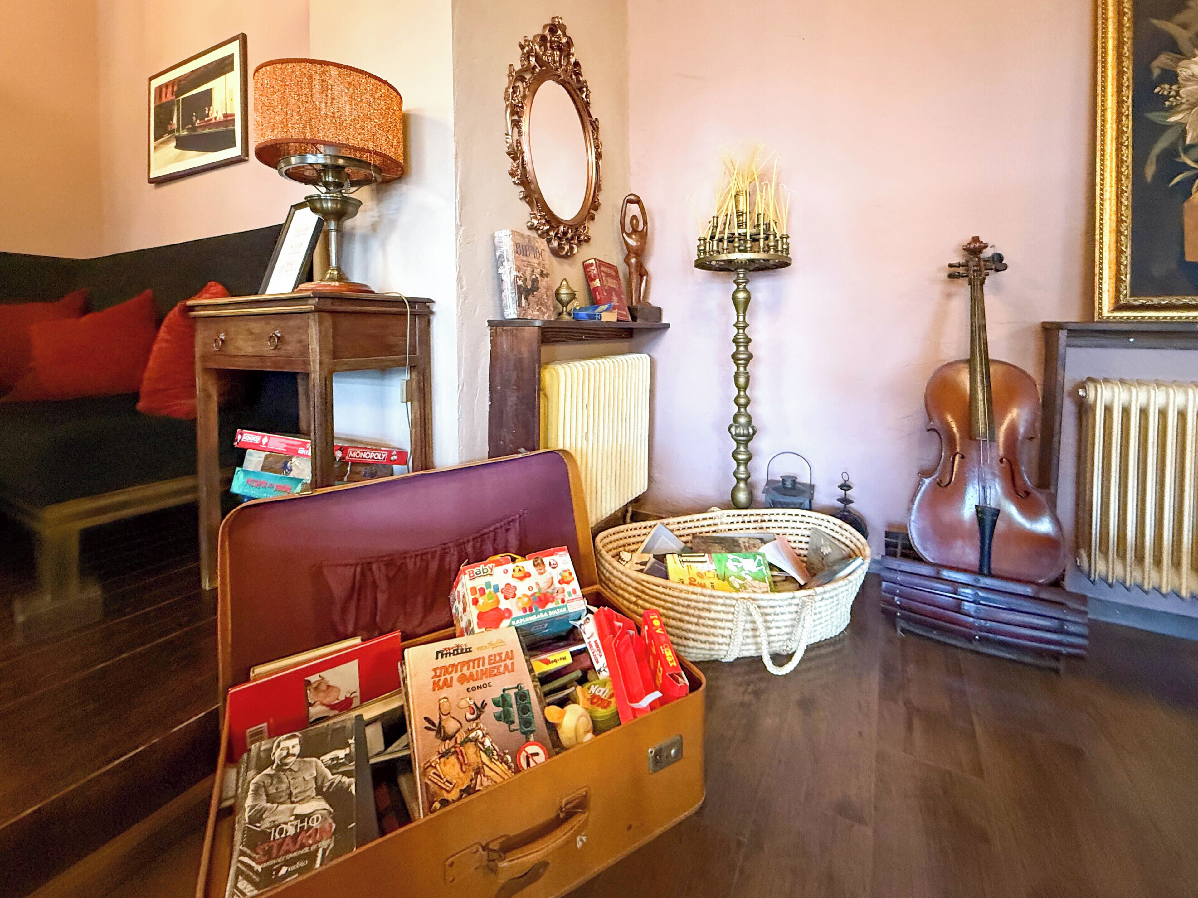 Un saló amb una maleta antiga plena de llibres i revistes, una taula de fusta amb una làmpada, un candelabre i un violí.