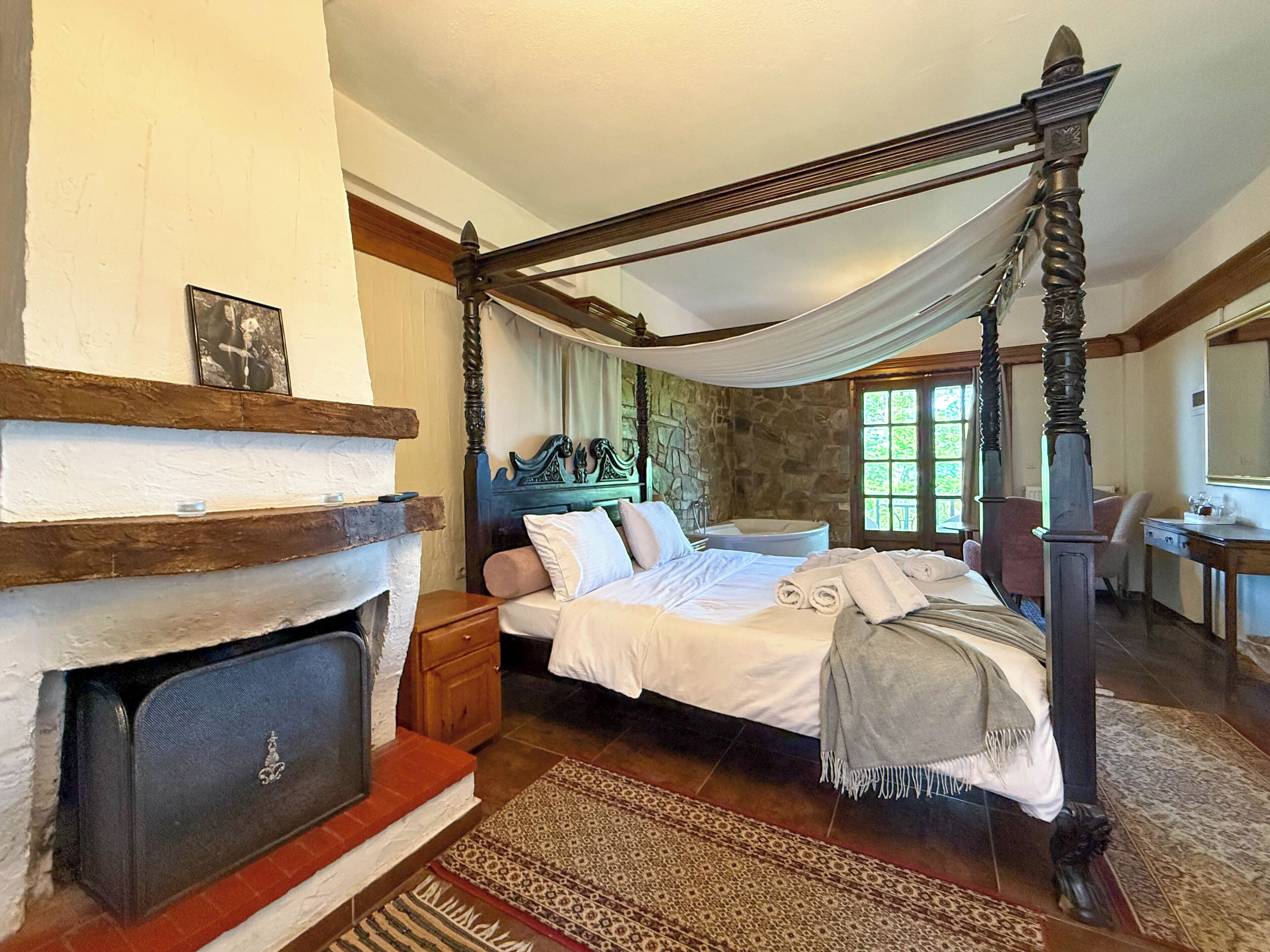 A traditional bedroom with a four-poster bed, a stone wall, a fireplace, and a large window.