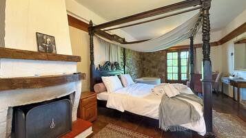A traditional bedroom with a four-poster bed, a stone wall, a fireplace, and a large window.
