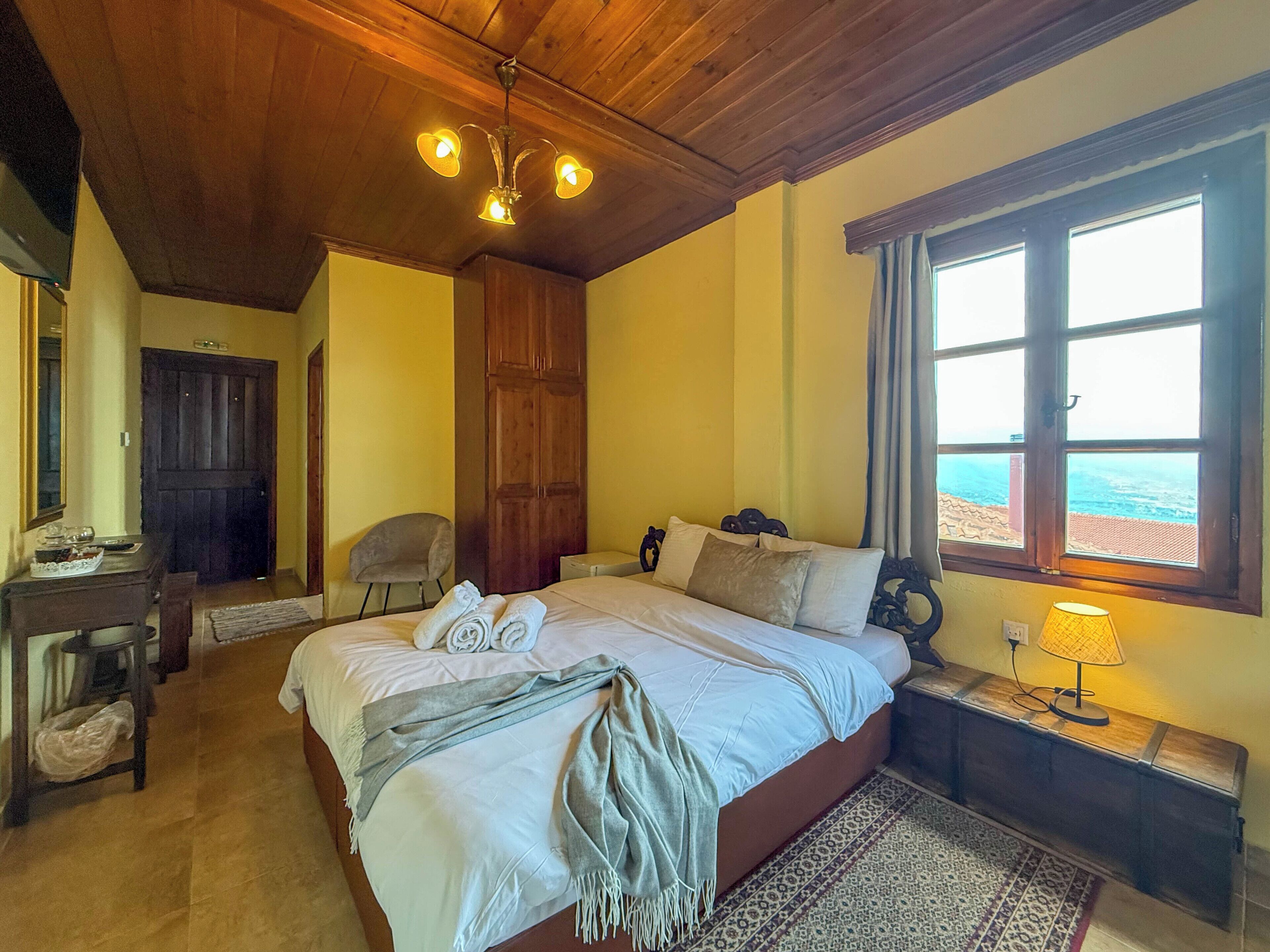 Une chambre à coucher comprenant un lit, un bureau, une chaise, une fenêtre avec vue et un lustre.