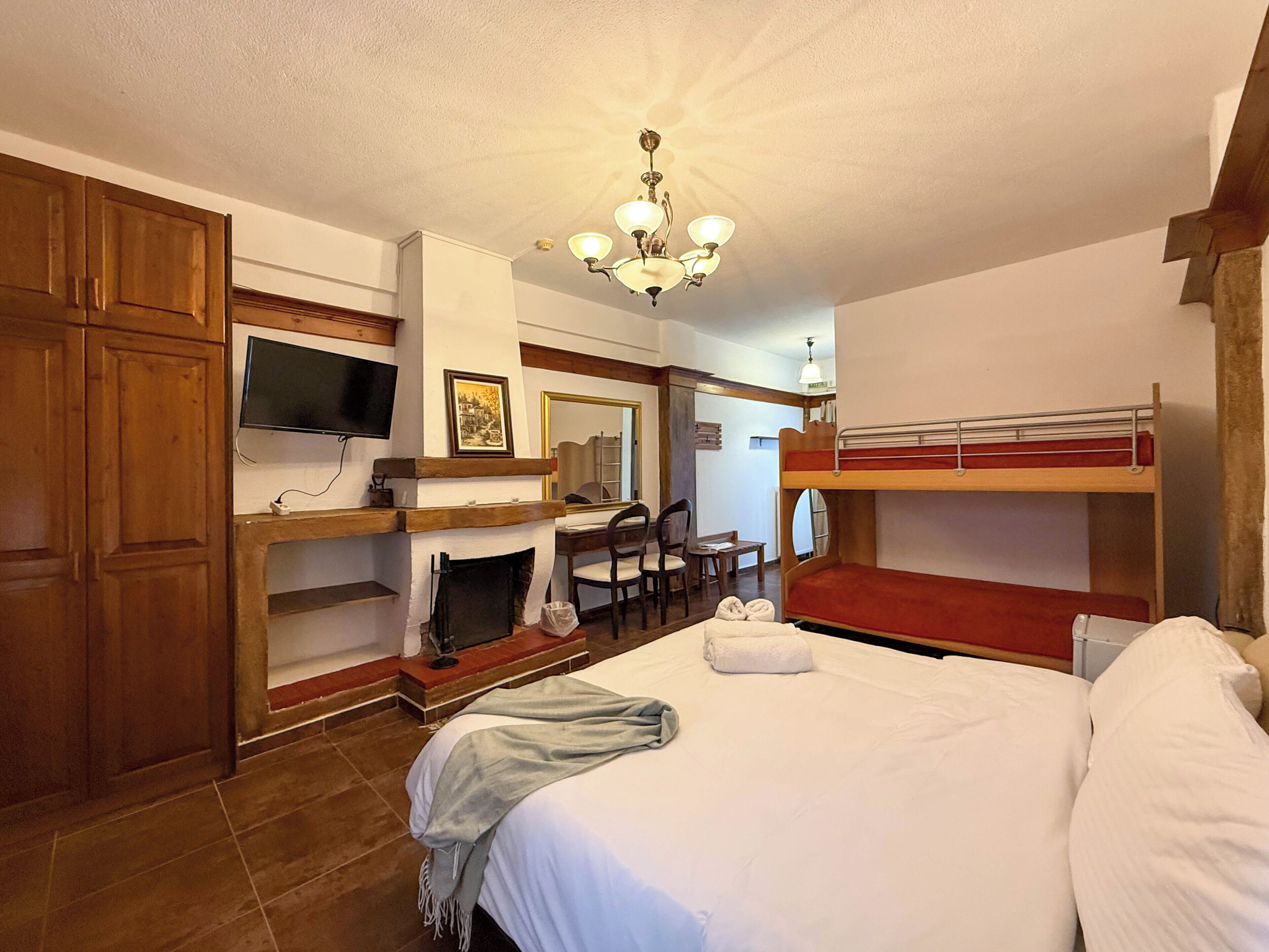 A hotel room with a bed, a desk, a chair, a television, a fireplace, and a bunk bed.