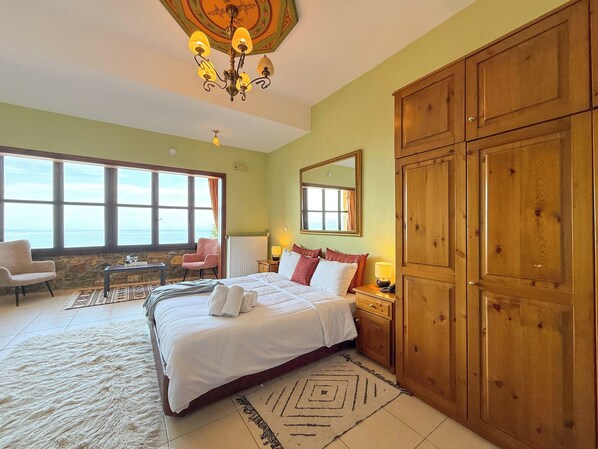 Une chambre avec un grand lit, une armoire en bois, un bureau avec une chaise, une fenêtre donnant sur un beau paysage et un lustre.