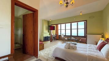 A bedroom with a bed, a TV, a window with a view, a wooden door, and a chandelier.