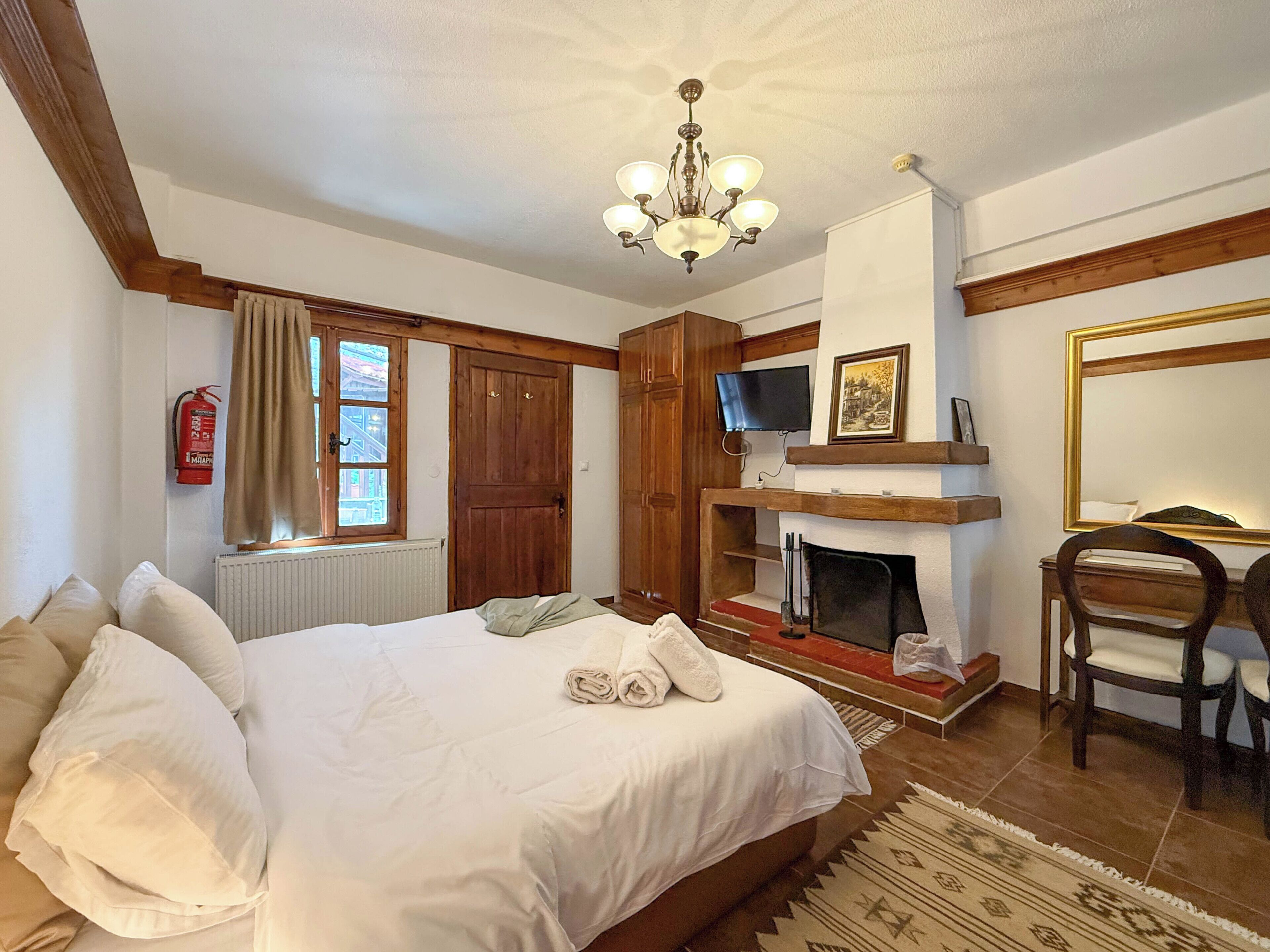 A bedroom with a bed, a fireplace, a television, and a mirror.