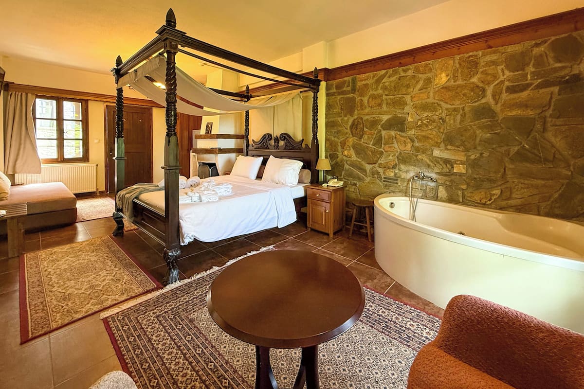 Un lit à baldaquin, un mur en pierre, une baignoire et une table ronde dans une chambre d’hôtel.