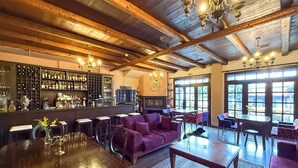 Un espace bar avec un plafond en bois, des tabourets de bar et une grande table. L’espace détente comprend des canapés violets et un téléviseur.