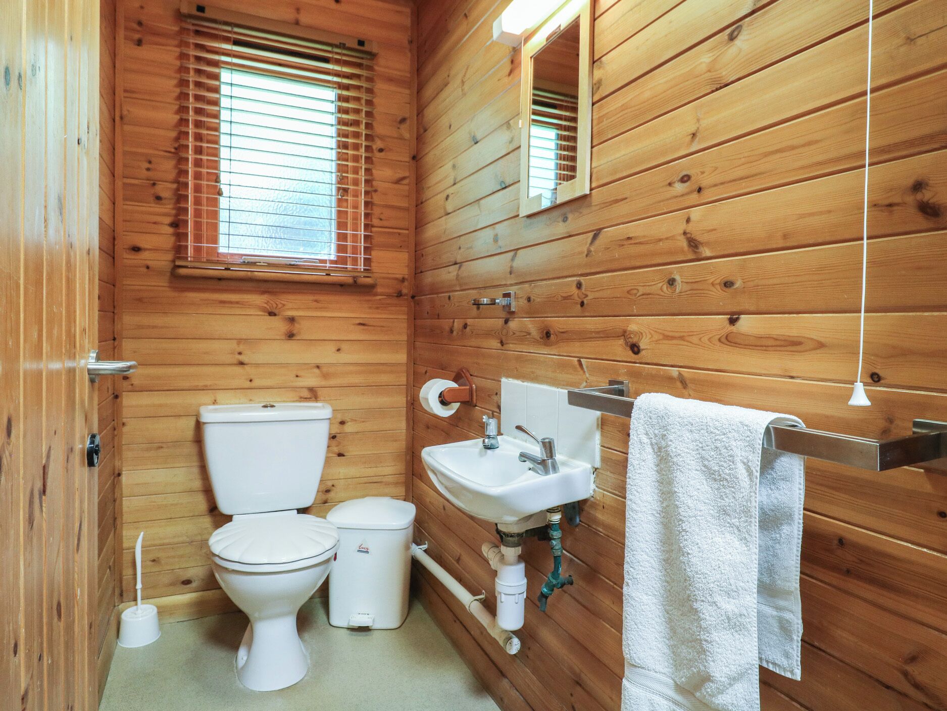 A wooden-paneled bathroom with a toilet, sink, and mirror.