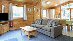 A cozy cabin interior with a sofa, a wooden coffee table, and a television. - Sycamore Lodge (Swadlincote)