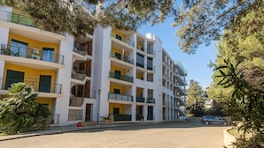 Un immeuble résidentiel à plusieurs étages, doté de balcons, d’une allée pavée et entouré de verdure.