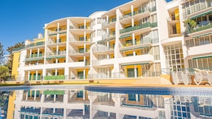 Un hôtel à plusieurs étages doté de balcons, d’une piscine et surplombant un ciel d’un bleu limpide.