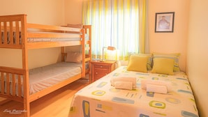 Une chambre avec un lit superposé, un lit simple et une table de chevet avec une lampe.
