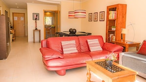 Un salon avec un canapé en cuir rouge, une table basse en bois sur laquelle est posé un jeu d’échecs, une bibliothèque et un coin repas avec une table et des chaises.
