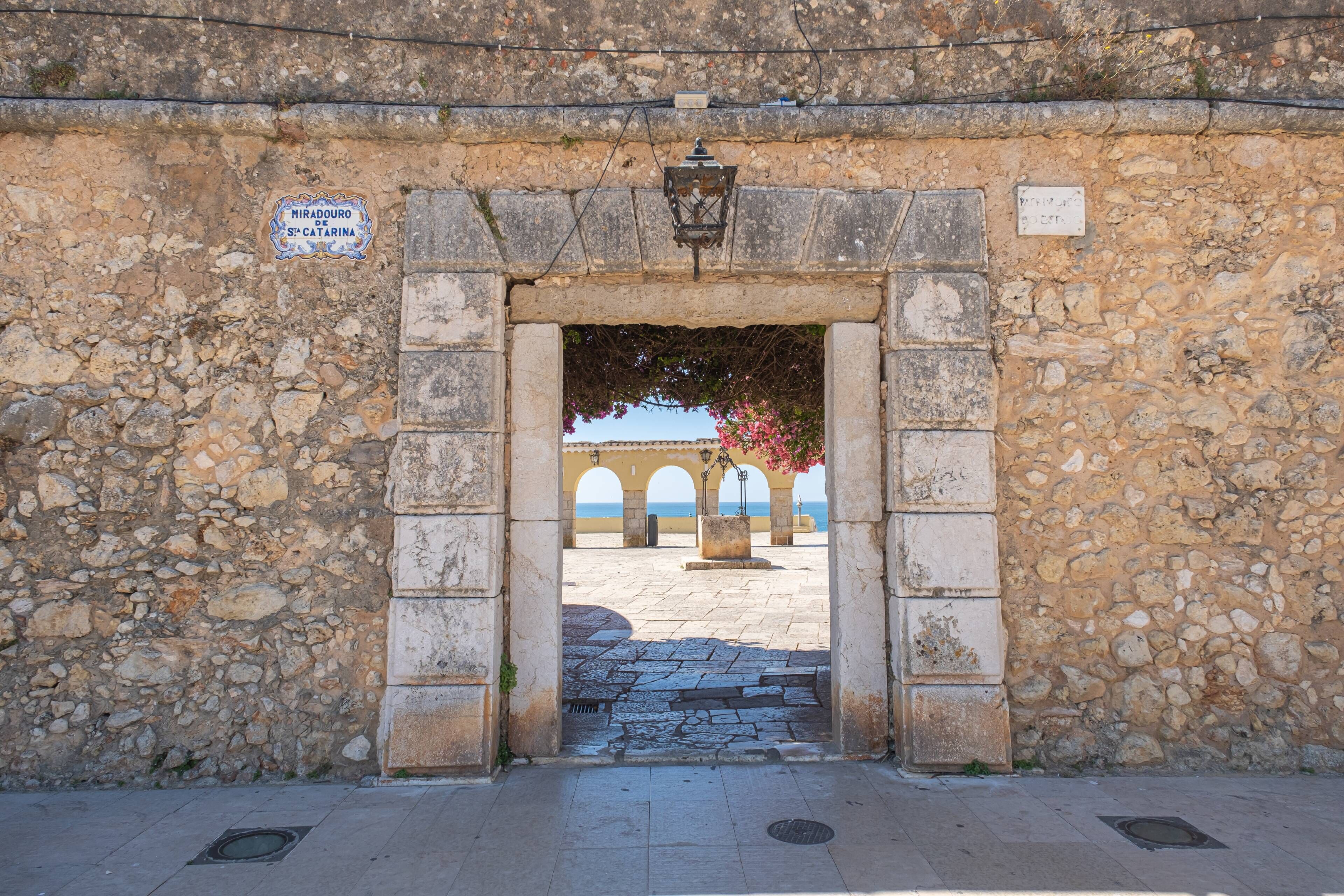 Um arco de pedra que dá acesso a um pátio com vista para o mar.