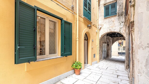 A narrow alleyway with a yellow building, green shutters, and a potted plant. - Ai Vicoli Ciambra's Alley - Suite Guglielmo by Wonderful Italy (Monreale)