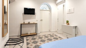 A modern bedroom with a bed, a TV mounted on the wall, a console table, a door with a fan, and a radiator. - Ai Vicoli Ciambra's Alley - Suite Guglielmo by Wonderful Italy (Monreale)