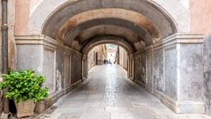 A narrow, arched corridor with stone walls and a tiled floor, leading to a distant view. - Ai Vicoli Ciambra's Alley - Suite Guglielmo by Wonderful Italy (Monreale)