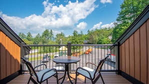 A balcony with a table and chairs, overlooking a parking area and a playground.