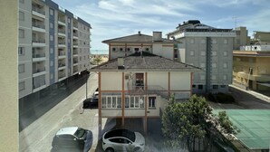 A residential building with a tiled roof, multiple balconies, and a parking area with two cars. - Seafront apartment in Bibione (Bibione)