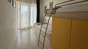 A room with a bunk bed, a ladder, a yellow wardrobe, and a window with sheer curtains. - Seafront apartment in Bibione (Bibione)