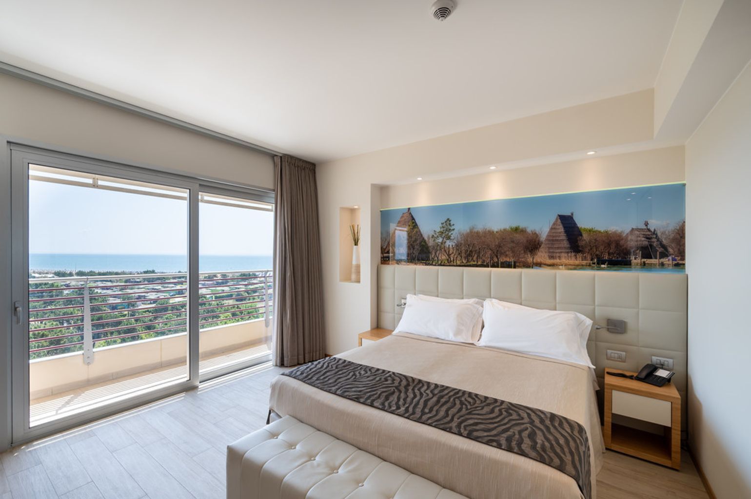Un dormitorio con una cama grande, vista de la ciudad a través de una puerta corrediza y un cuadro de un edificio tradicional en la pared.