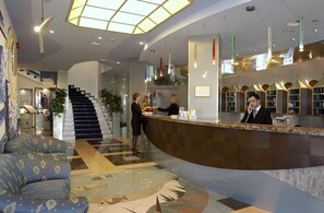 A hotel lobby with a reception desk, a staircase, and a seating area.