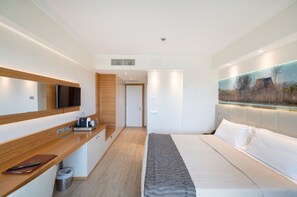 Une chambre d’hôtel moderne équipée d’un lit, d’un bureau avec un ordinateur, d’une télévision et d’un tableau représentant un paysage.