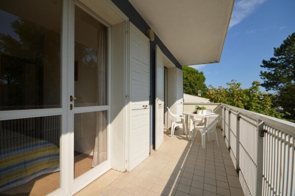 A balcony with a white railing, a small table with chairs, and a sliding glass door leading to a room.